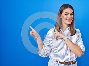 Hispanic young woman standing over blue background smiling and looking at the camera pointing with two hands and fingers to the