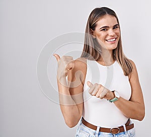 Hispanic young woman standing over white background pointing to the back behind with hand and thumbs up, smiling confident