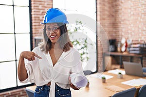 Hispanic young woman wearing architect hardhat at office pointing finger to one self smiling happy and proud