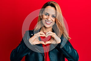 Hispanic young woman wearing black leather jacket smiling in love doing heart symbol shape with hands