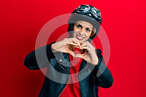 Hispanic young woman wearing motorcycle helmet smiling in love showing heart symbol and shape with hands