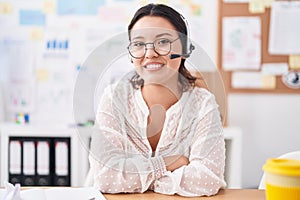 Hispanic young woman working at the office wearing headset and glasses happy face smiling with crossed arms looking at the camera