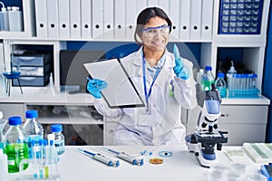 Hispanic young woman working at scientist laboratory pointing fingers to camera with happy and funny face