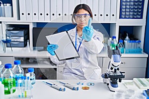 Hispanic young woman working at scientist laboratory showing middle finger, impolite and rude fuck off expression
