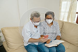 Hispanics wear masks while sitting on the couch with a cell phone