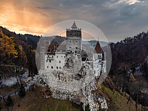 Historic Bran Castle (Dracula's Castle) surrounded by a forest against a sunset sky