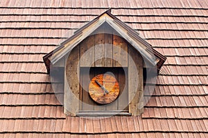 historic dormer with a wooden clock on a shingled roof