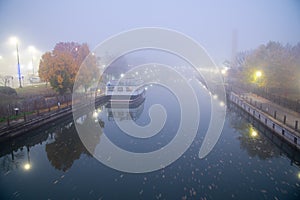 Historic Erie Canal in Fairport village with barge cruise boat tour, foggy morning mist and reflection of colorful fall foliage