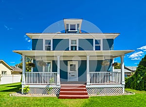 Historic family house with green lawn in front and blue sky background.