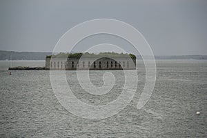 Historic Fort Gorges, with green vegetation on the roof, in Casco Bay on a cloudy day