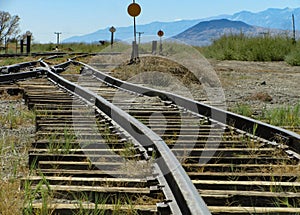 Narrow gauge railroad tracks run toward a switch junction and signals in an old train yard