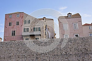 Historic pastel-colored buildings rise above the fortified stone walls of Dubrovnik, Croatia, under a clear and blue sky