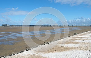 historic pier at southport merseyside with the beach at low tide and summer sky reflected in water on the beach