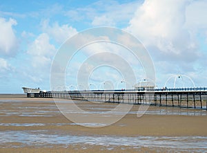 Historic pier at southport merseyside with the beach at low tide and summer sky reflected in water on the beach