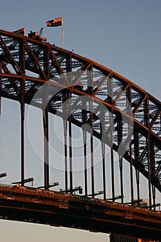 Historic steel truss arch bridge with crane and New South Wales flag on top. Iconic Sydney Harbor Bridge at dusk, Australia.