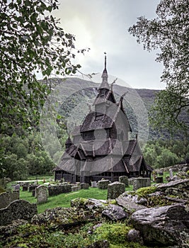 Historical Borgund stave church in Norway with surrounding cemetery and framed by trees.
