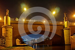 Historical bridge over a river with city lights and christian sculptures at night