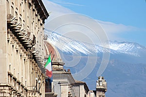 Historical building in Catania, Sicily, Italy with waving Italian flag. In the background cupola of famous Saint Agatha Cathedral