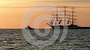 Historical tall ship replica schooner floats past the lighthouse at sea near a smaller towing boat