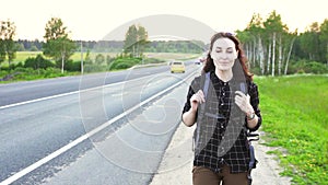 Hitchhiker girl with a tourist backpack walking on the road