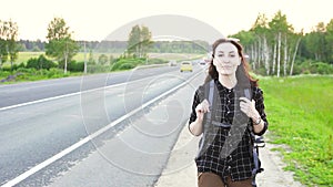 Hitchhiker girl with a tourist backpack walking on the road