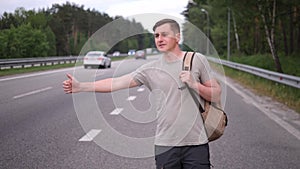 Hitchhiker, a man with a backpack stands by the road and stops cars, thumbs up