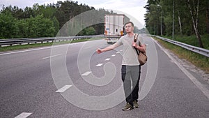 Hitchhiker, a man with a backpack stands by the road and stops cars, thumbs up