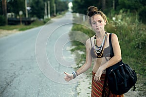 A hitchhiking girl stands voting on a country road