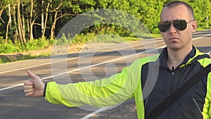 Hitchhiking traveling young adult man pointing thumb up on interstate highway