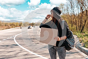 Hitchhiking. Young caucasian woman in sunglasses and cap holding a cardboard sign with mock up. Copy space. The concept