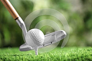 Hitting golf ball with club on artificial grass against blurred background, space for