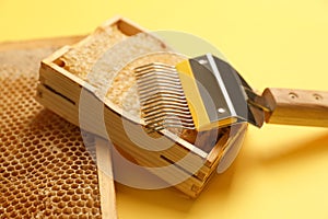 Hive frames with honeycombs and uncapping fork on yellow background, closeup. Beekeeping