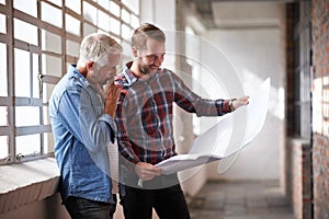 Hm, where to begin. two male architects discussing blueprints while standing indoors.