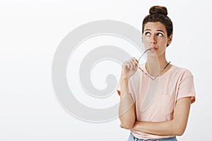 Hmm might work. Portrait of unsure hesitant cute tanned female with messy bun biting frame of eyewear gazing at upper photo