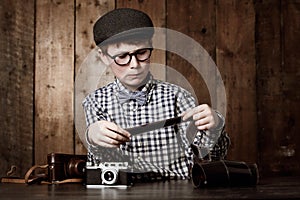 Hmm, these will develop well. Young boy in retro clothing wearing spectacles and checking a photographic negative.