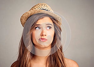 Hmmm...what to do. Studio shot of an attractive young woman looking unsure against a gray background.