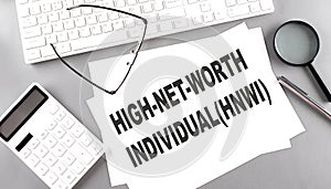 HNWI high net worth individuals text on paper with keyboard, calculator on grey background