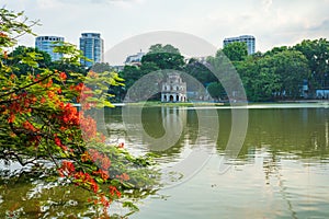 Hoan Kiem lake with Turtle Tower and flamboyant flowers on foreground in Hanoi, Vietnam