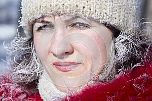 A girl in a red jacket and a white knitted hat in the winter in the cold. Hoarfrost on hair and eyelashes