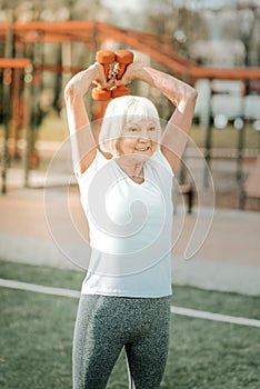 Hoary energetic sportswoman engaging in arms exercises with weights