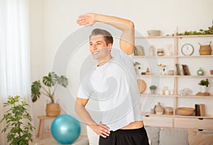 Hobbies in free time and healthy lifestyle. Attractive man smiling and doing exercises in living room