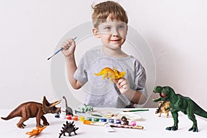 Hobby: a boy, a preschooler, paints with a brush and a tassel a small figure of a dinosaur toy.