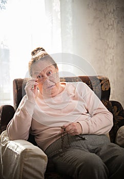 Hobby. An elderly caucasian woman in glasses enjoys her hobby sitting in a armchair and knitting on the background of