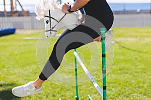 Hobby horsing competition on a green grass, hobby horse riders jumping, equestrian sport training with stick toy horses in a