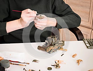 Hobby and leisure concept. Teen boy assembling and painting plastic models of soldiers and tank at workplace in his room.