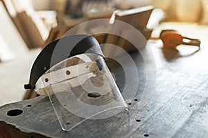 Hobby wood concept. Photo of cabinetmaker protective face mask lying on the black table with headset and lumber plank on blurred