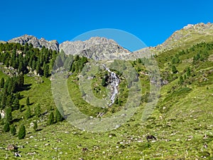 Hochschober - Horses grazing on alpine meadow with scenic view of idyllic waterfall and majestic mountain peak of Hochschober