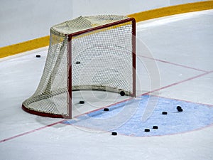 Hockey gates on ice close-up. Several pucks are visible near the goal and behind the net.