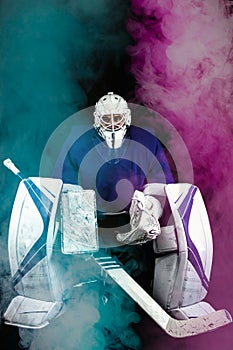 Hockey goalie in complete hockey outfit sitting on office chair. Around him is blue and pink smoke.