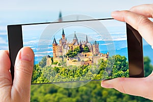 Hohenzollern Castle on mountain top, Germany. Tourist taking photo of famous castle by cell phone
